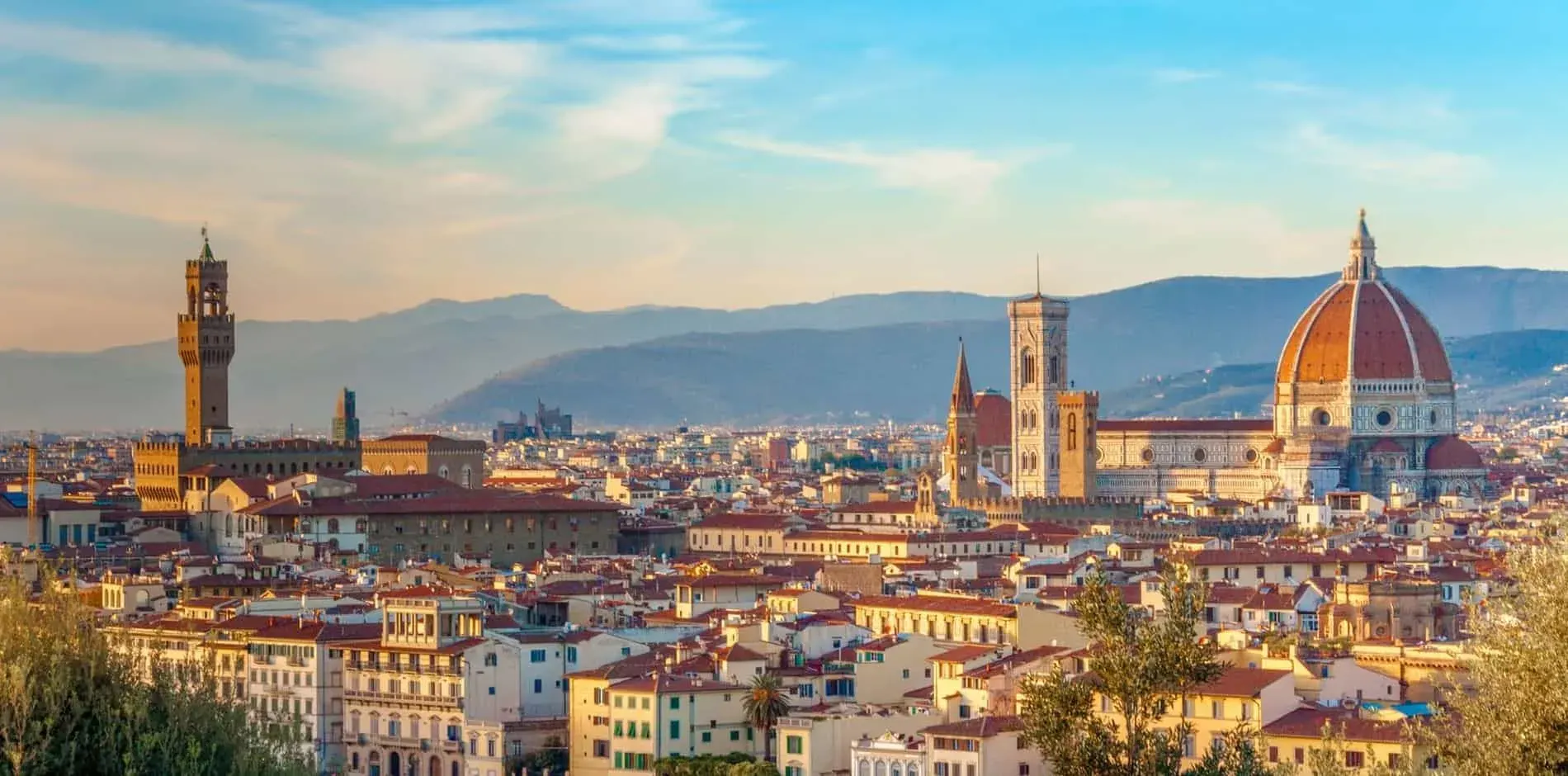 Panoramic view of a historic Italian city with a red-domed cathedral, a bell tower and terracotta rooftops under a soft sky